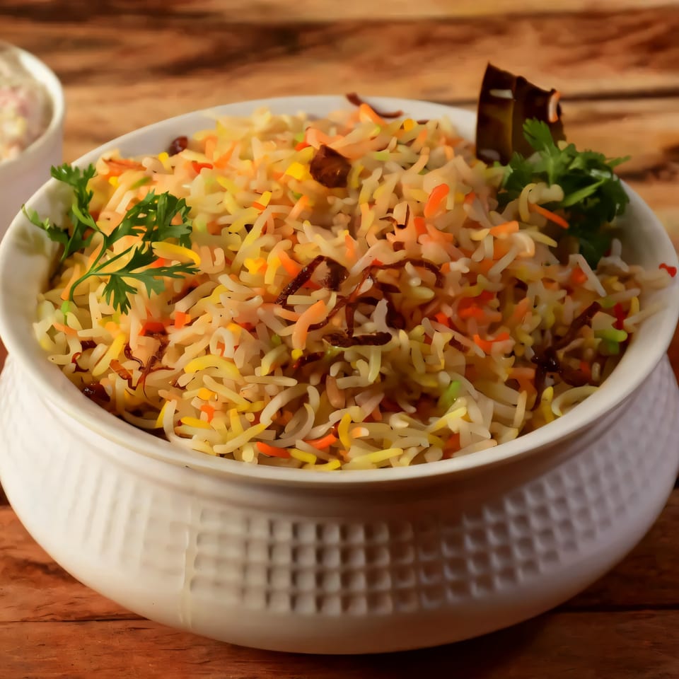 Colorful Indian biryani rice with herbs and spices in a white bowl on a wooden table.